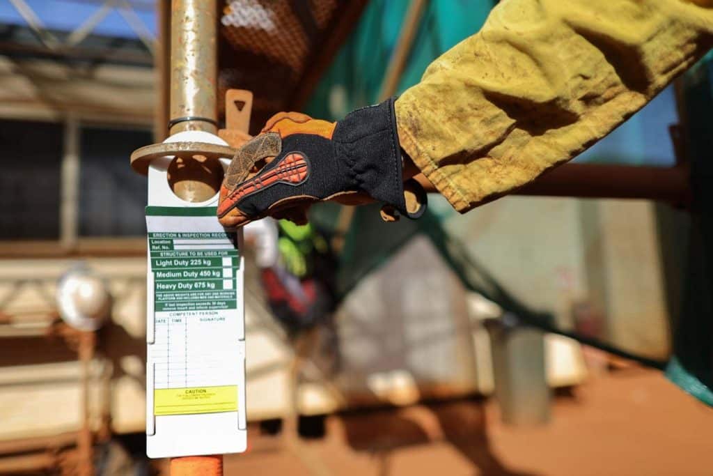 A green scaffold tag with white background is shown in this job site photo.