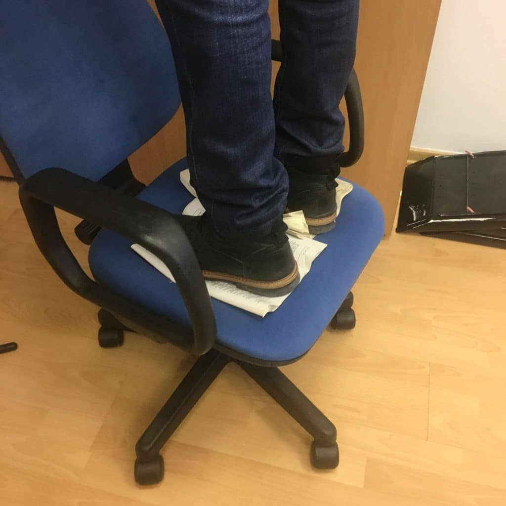 A person stands on a wheeled desk chair - an accident waiting to happen. Avoid accidents by using 1st Reporting for your safety inspections.