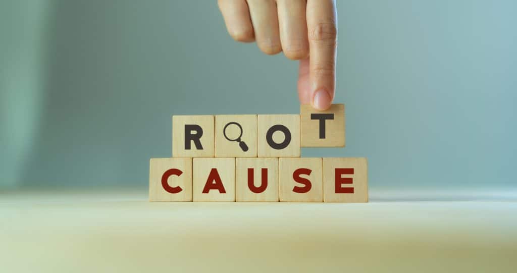 A hand places blocks spelling 'root cause', symbolic for a root cause analysis. Learn more about root cause analysis reporting at 1stReporting.com.