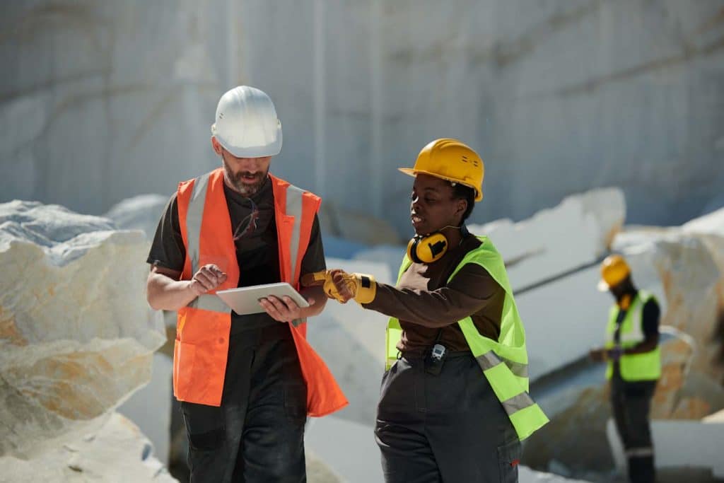 A construction worker shows another worker elements of the digital construction submittal log on a tablet. Learn more about construction reporting at 1stReporting.com.