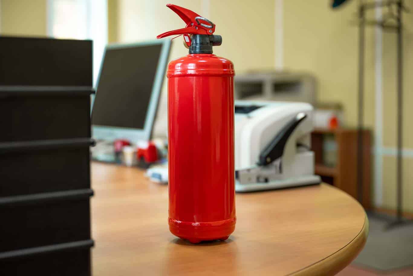 A fire extinguisher on a desk in an office - a useful fire safety resource. Learn more about fire safety at 1stReporting.com.